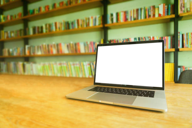 istock Notebook laptop with white blank screen on wooden table in library room or home office. 1060020156
