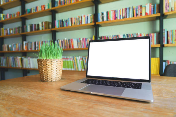 istock Notebook laptop with white blank screen on wooden table in library room or home office. 1060020192