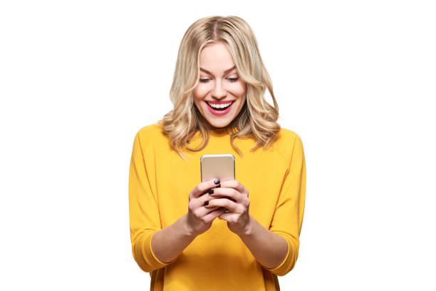 Excited young woman looking at her mobile phone smiling. Woman reading text message on her phone, isolated over white background. stock photo