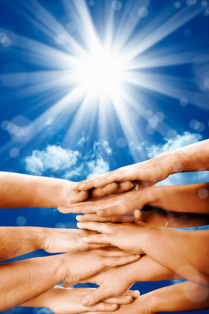 istock group of hands clasped together over blue sky with light beam 1060024694