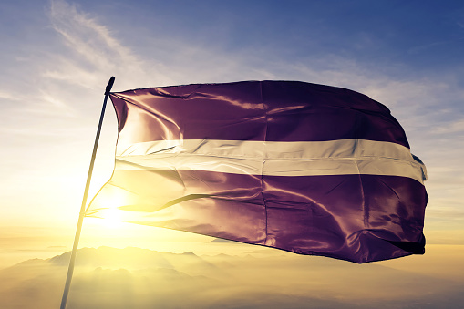 Letonia Letonia bandera tela tela ondeando en la niebla de la niebla de amanecer superior photo