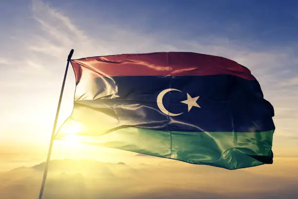 Libya Libyan flag on flagpole textile cloth fabric waving on the top sunrise mist fog