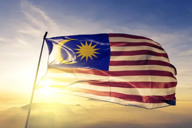 Malaysia Malaysian  flag on flagpole textile cloth fabric waving on the top sunrise mist fog