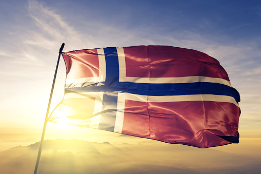 Norway Norwegian flag on flagpole textile cloth fabric waving on the top sunrise mist fog