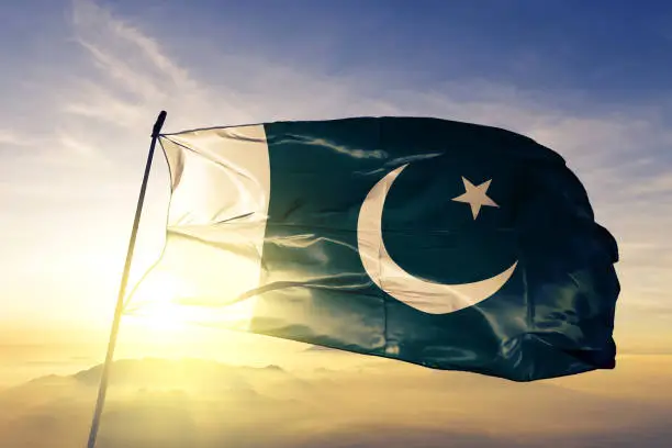 Pakistan Pakistani flag on flagpole textile cloth fabric waving on the top sunrise mist fog