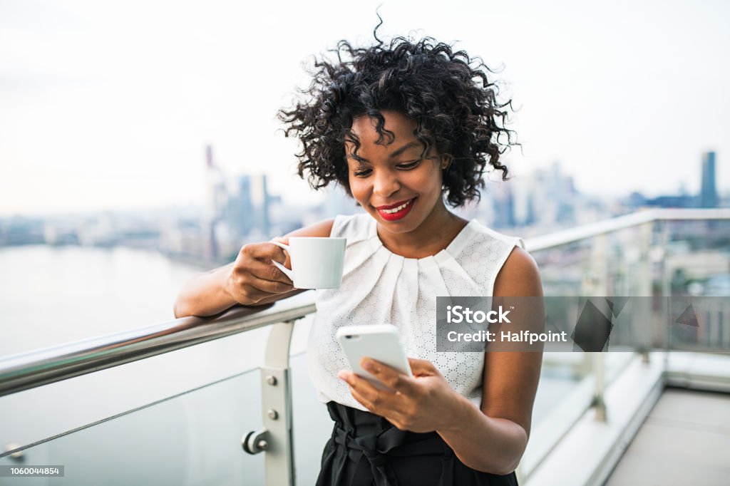 A businesswoman with coffee and smartphone standing against London view panorama. A businesswoman with coffee and smartphone standing against London view panorama, text messaging. Women Stock Photo