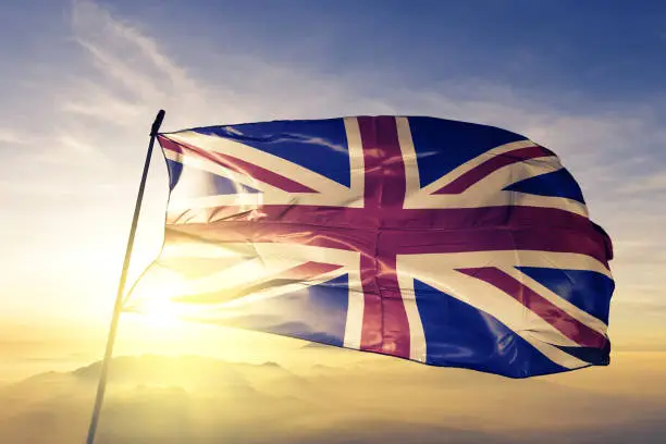 Photo of United Kingdom British english flag textile cloth fabric waving on the top sunrise mist fog