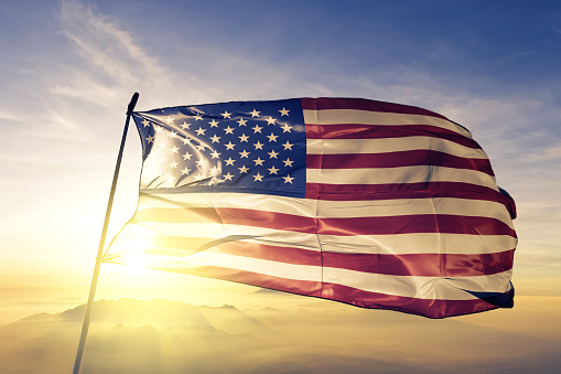 United States american usa us flag on flagpole textile cloth fabric waving on the top sunrise mist fog