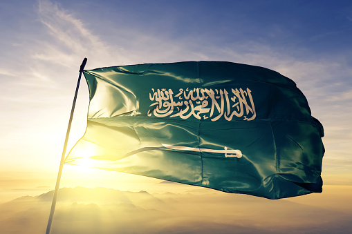 Saudi Arabia Arabian flag on flagpole textile cloth fabric waving on the top sunrise mist fog