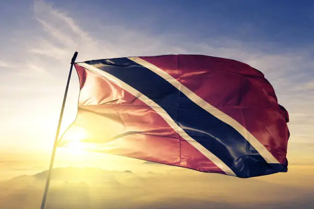 Photo of Trinidad and Tobago flag textile cloth fabric waving on the top sunrise mist fog