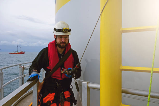 Offshore manual high workers looking at camera and preparing for climbing ladder from wind turbine - platform.