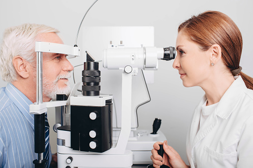 Doctor Optometrist examining old man's eyes with special eye equipment