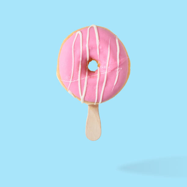 istock Pink glazed donut with ice cream stick on blue pastel background 1060094034