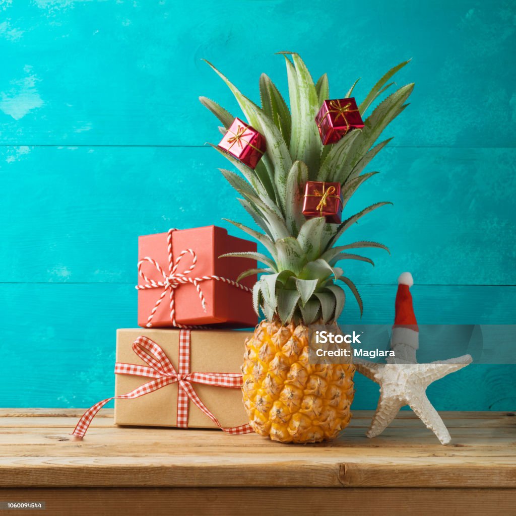 Christmas holiday concept with  pineapple as alternative Christmas tree and gift boxes on wooden table with copy space Pineapple Stock Photo
