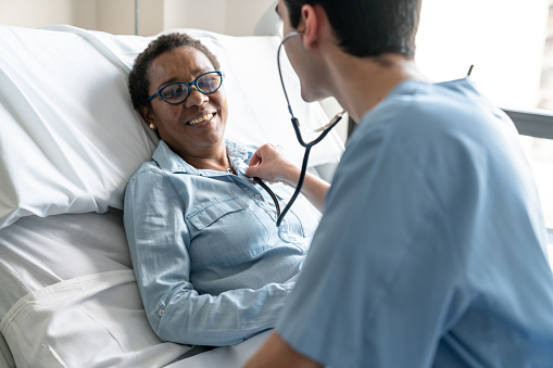 Paciente femenino negro acostado en cama de hospital, mientras que la enfermera es verificar su corazón latir con estetoscopio photo