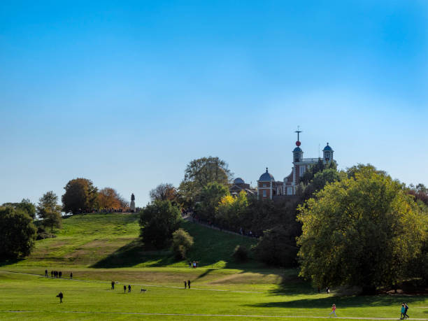 People and dogs enjoying the sunshine on a lovely autumn day in Greenwich Park, London. The Royal Observatory, home of the Greenwich Meridian, is at the top of the hill with a statue of General James Wolfe silhouetted against the sky. An observation point in front of the statue allows tourists a spectacular view over London Docklands, the River Thames and the City of London.