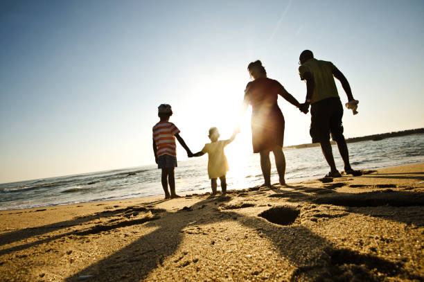 Hand In Hand Together In Unity: Silhouette Of A Young Family (Kids) On A Colourful Beachside stock photo