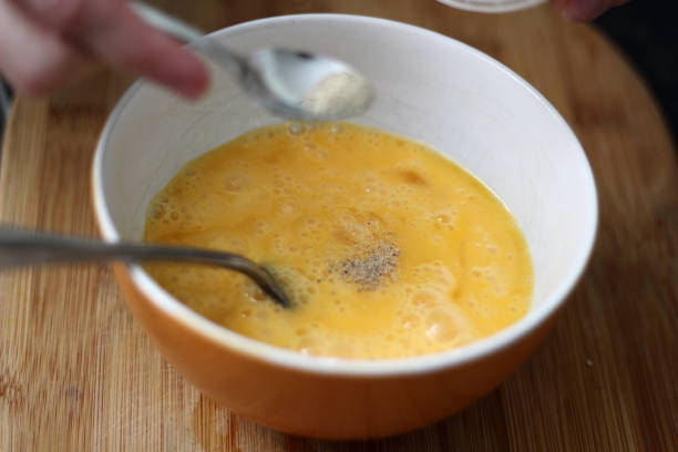 istock Adding white ground pepper into beaten eggs in bowl. Making omelette series. 1060144066