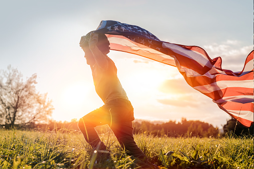 Little boy running with American flag at sunset