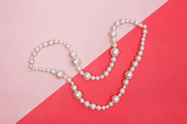 Shiny pearl necklace on pink background, looking like a smile.