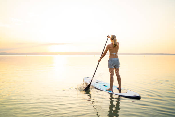 rear view 44 years old woman on stand up paddle board paddling in lake in bright sunlight alone summer place for text