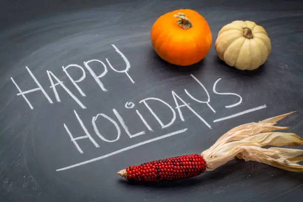 Happy Holidays greeting card - white chalk handwriting on a slate blackboard with a pumpkin, gourd and corn