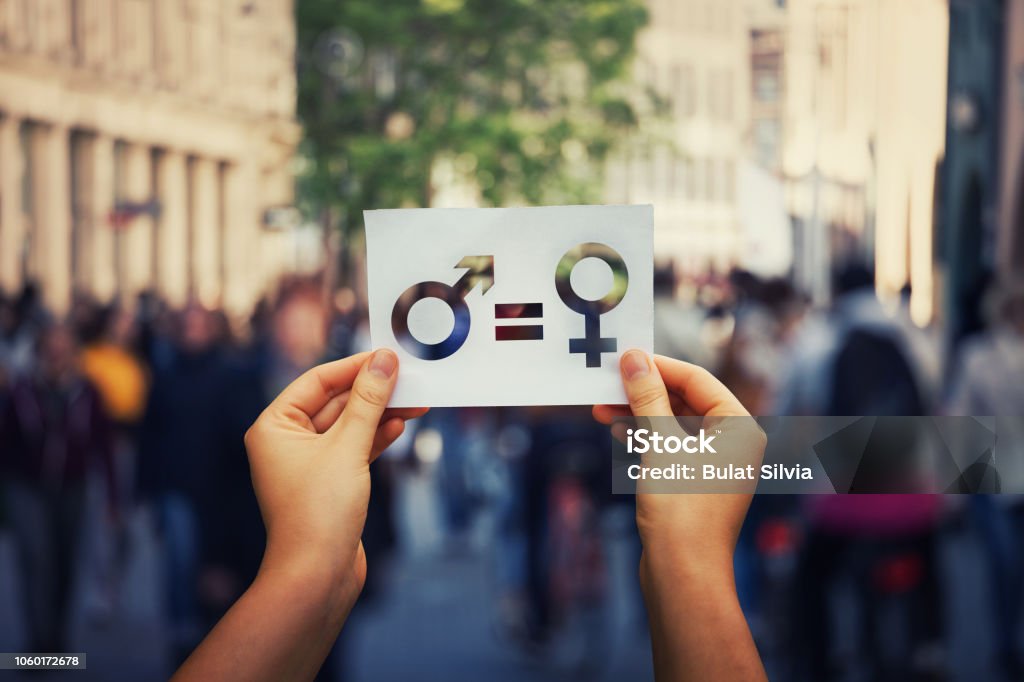 Sex sign as a metaphor of social issue Gender equality concept as woman hands holding a white paper sheet with male and female symbol over a crowded city street background. Sex sign as a metaphor of social issue. Gender Equality Stock Photo