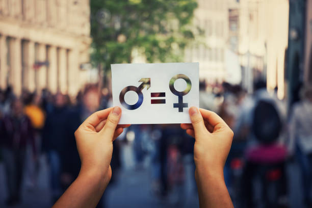 Sex sign as a metaphor of social issue Gender equality concept as woman hands holding a white paper sheet with male and female symbol over a crowded city street background. Sex sign as a metaphor of social issue. gender equality stock pictures, royalty-free photos & images