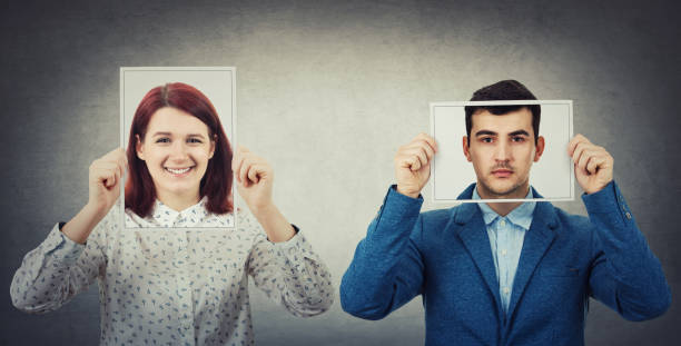 Introvert vs extrovert. Businessman and woman covering their faces using photo sheets with happy and sad portrait emoticon, like a mask to hide the real emotion from society. Fake identity concept. Introvert vs extrovert. person holding frame over face stock pictures, royalty-free photos & images