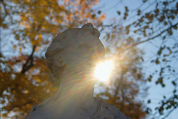 The autumn sun shines from behind the statue in the Park. Horizontal.