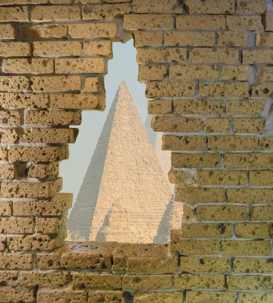 istock Old yellow brick wall in ruins with a big opening in it viewing on some egyptian pyramids 1060202284