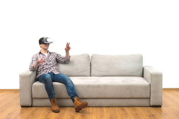 The man in virtual glasses gesturing on the sofa on the white wall background