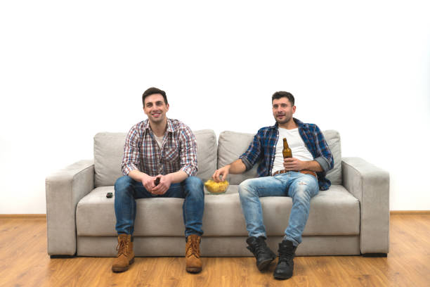 istock The two men drink a beer on the sofa on a white wall background 1060203848