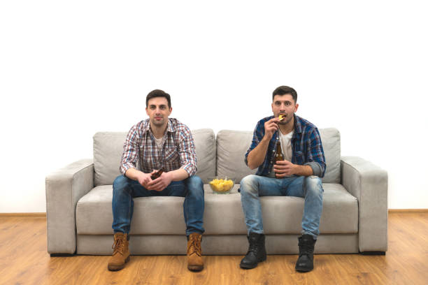 istock The two men drink a beer on the sofa on a white wall background 1060203850