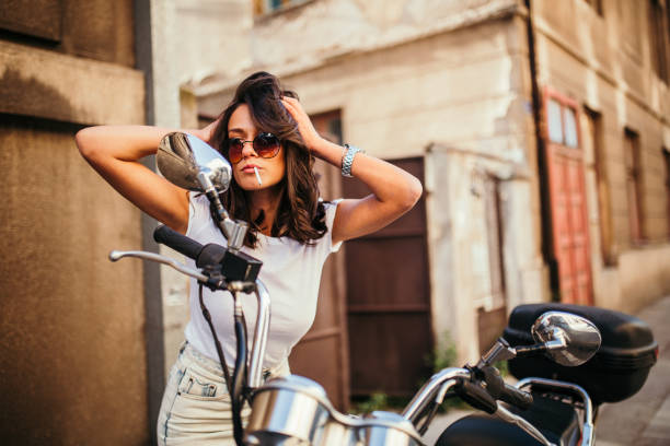 istock Young pretty fashioned girl smoking and looking at her reflection in motorcycle mirror 1060204542