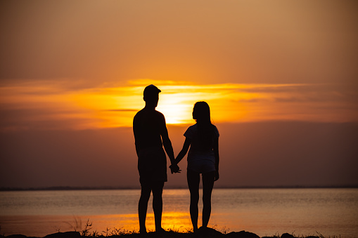 The couple standing near a water on the sunrise background