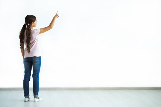 The little girl gesturing on the white wall background stock photo