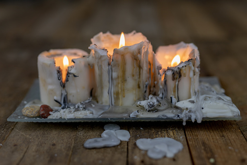 Old candles with dirty wax on a wooden table. Burning dirty candlesticks on a glass stand. Dark background.