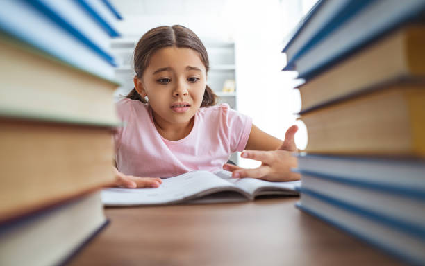 The angry schoolgirl sitting on the desk with books stock photo