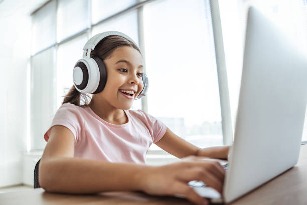 The happy girl in headphones with a laptop sitting at the table stock photo