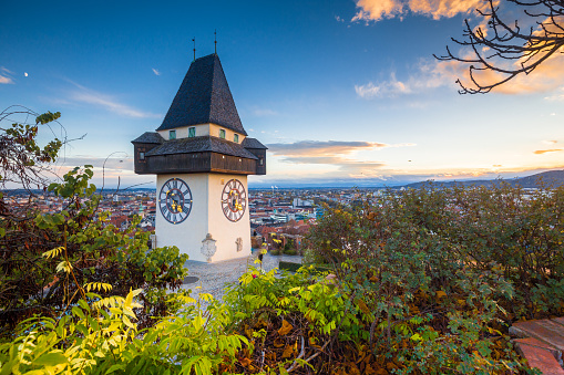 Classic panorama view of the historic city of Graz with famous Grazer Uhrturm clock tower in beautiful evening light at sunset, Styria, Austria