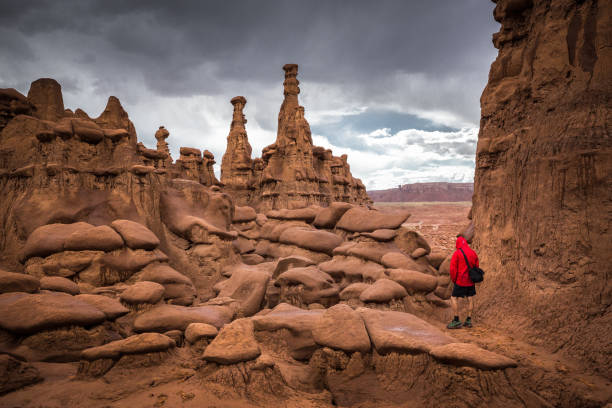 Panoramic view of hiker in red jacket standing in Goblin Valley State Park amidst beautiful hoodoos sandstone formations, Utah, USA