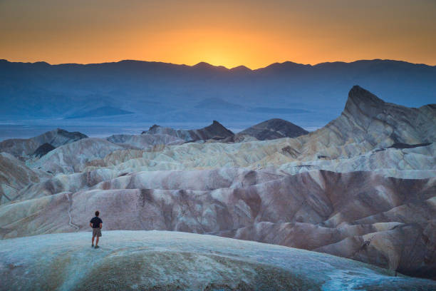 Hiker enjoying sunset at Zabriskie Point, Death Valley National Park, California, USA Classic panoramic view of male hiker standing at famous Zabriskie Point viewpoint in beautiful golden evening light at sunset in summer, Death Valley National Park, California, USA death valley national park stock pictures, royalty-free photos & images