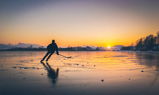 Hockey player skating on a frozen lake at sunset
