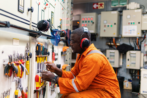 African marine engineer officer in engine control room ECR. He works in workshop and chooses correct tools and equipment