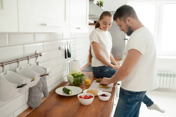 istock Young girlfriend sitting on tabletop watching boyfriend cooking breakfast 1060280828