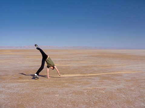 Man jumping and rolling into a cartwheel with one leg up and head upsidedown at Chott el Jarid. Desert and salt lake on the background