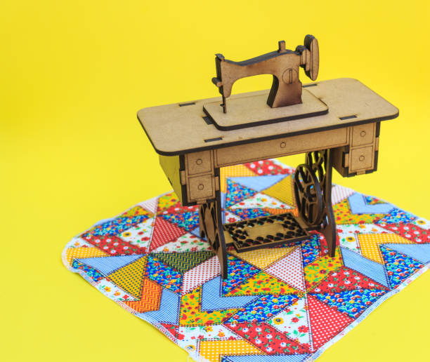 istock Mini sewing machine, made of wood, on a patchwork rug, with yellow background. 1060311764