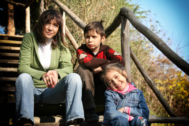 mother and children portrait of young adult woman with little girl and teenage boy sitting front of wooden house - 2640 imagens e fotografias de stock