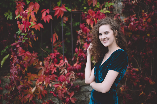 Beautiful smiling brunette in a stylish dark blue velvet dress in an autumn park